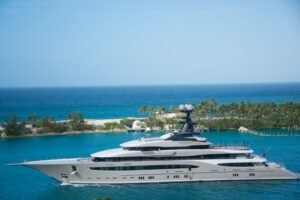 High-end yacht cruising along a tropical coastline with clear blue waters and lush greenery.
