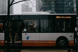Modern bus with number and inscription on roadway against multistory building facades in city