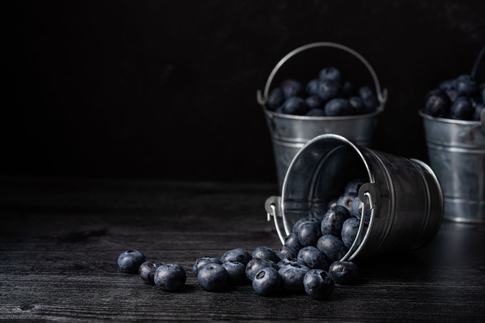 Fresh blueberries spilling out from a metal bucket with more in the background, highlighting a rustic harvest theme.