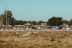 View of Francistown's urban landscape showcasing parked cars and a person walking in a grassy area.