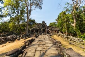 Scenic view of ancient Angkor Wat temple ruins amidst lush greenery under a bright sky.