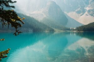 A breathtaking view of a turquoise lake surrounded by lush forests and towering mountains.
