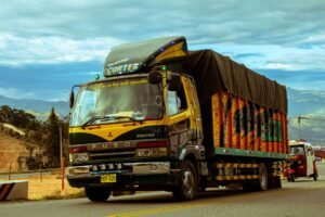 Vibrant cargo truck cruising a scenic mountain highway under a dramatic sky.