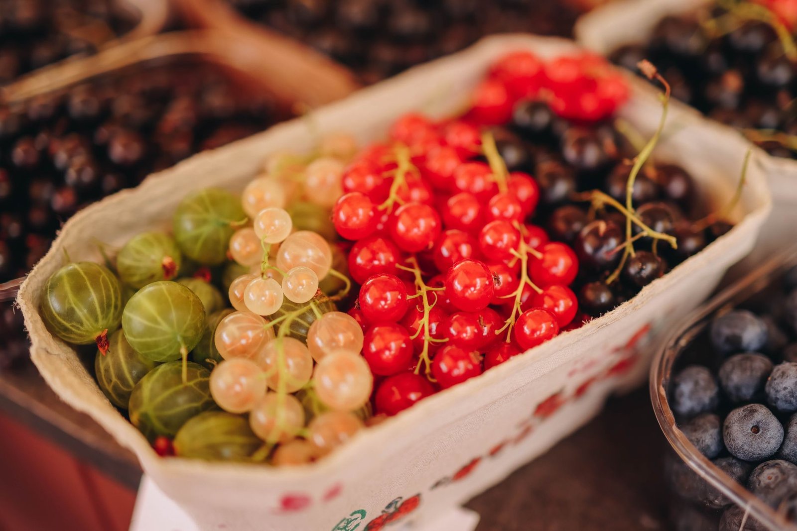 Vibrant close-up of fresh berries including currants and gooseberries at an outdoor market.