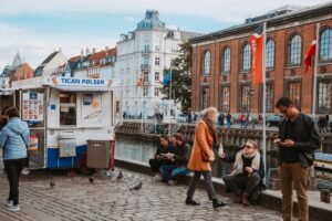 Candid street scene by Copenhagen canal with locals enjoying street food and sightseeing.