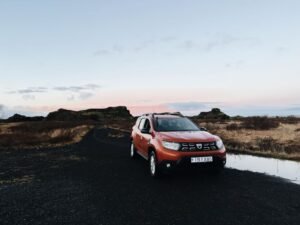 An orange SUV parked on a dirt road in Iceland's countryside at sunset.