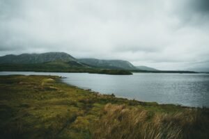 Tranquil landscape featuring a serene lake, mountains, and cloudy skies.