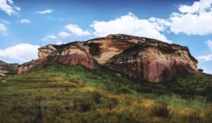 Stunning rock formation with vibrant colors and grassy foreground under a blue sky.