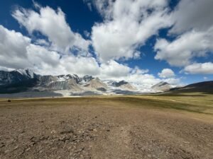 Panoramic view of Altai Mountains with majestic glaciers under a bright blue sky with fluffy clouds.