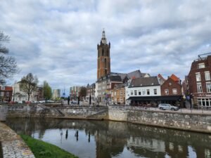 Beautiful cityscape with church tower, canal, and historic buildings under a cloudy sky.
