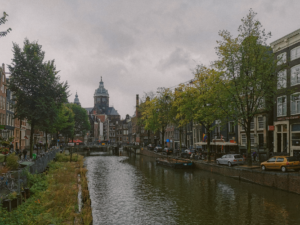 Scenic view of Amsterdam's canal with historic buildings and cathedral on a cloudy day.