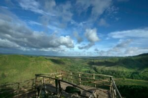 A wooden observation deck overlooking lush green hills under a bright blue sky.