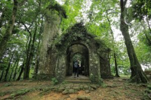 A traveler explores a historic stone structure surrounded by vibrant forests in Vietnam.