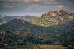 Aerial view of lush, rocky hills in Zimbabwe under a cloudy sky, showcasing natural beauty.